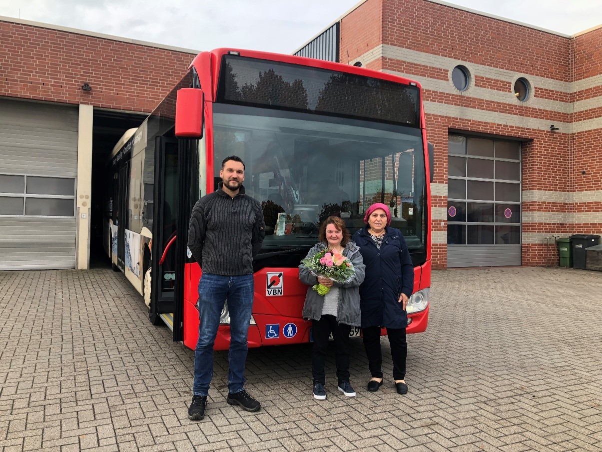 Moritz Bruckhoff bei der Blumenübergabe mit Yasa Erdem und Gülüsan Dalgic vor einem AllerBus-Linienbus.
